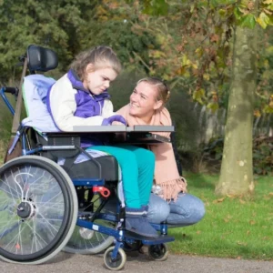 A woman and girl in a wheelchair on the side of road.