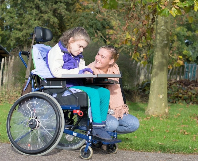 A woman and girl in a wheelchair on the side of road.