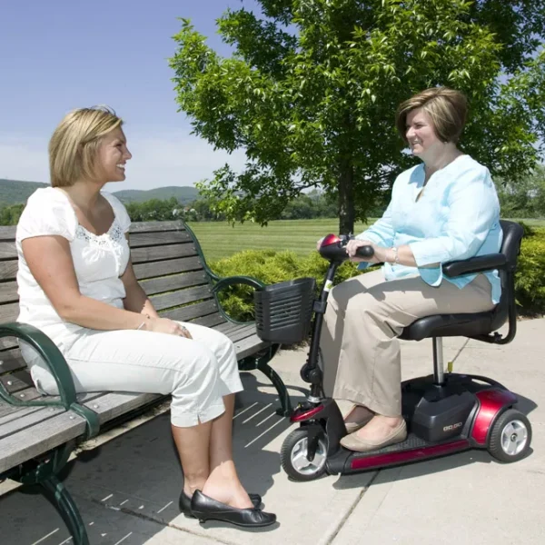 Two women sitting on a bench with a scooter.