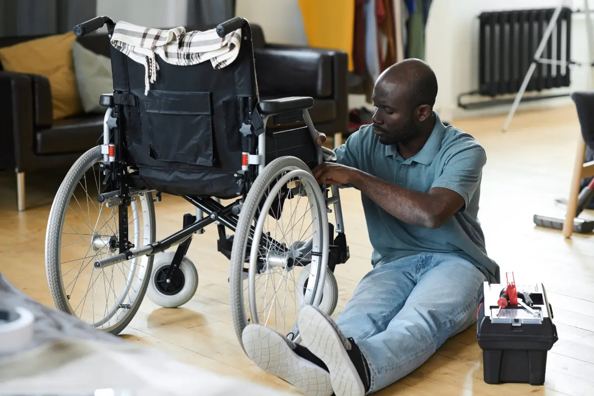 A man sitting on the floor next to a wheelchair.