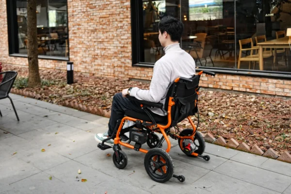 A man sitting in an orange wheelchair on the sidewalk.