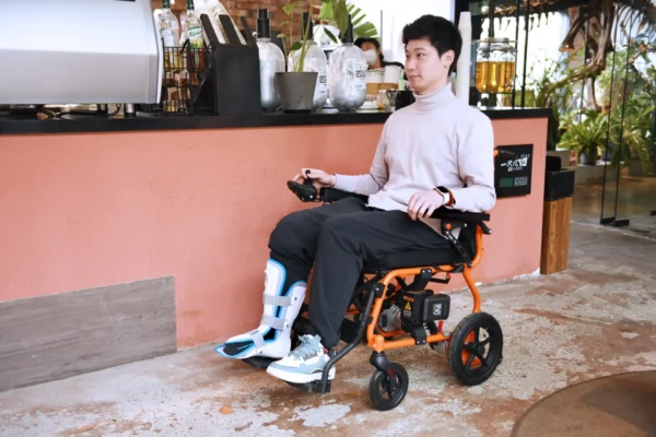 A man sitting in an orange wheelchair with a remote control.