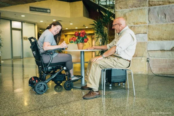 A woman in a wheelchair and an older man sitting at a table.